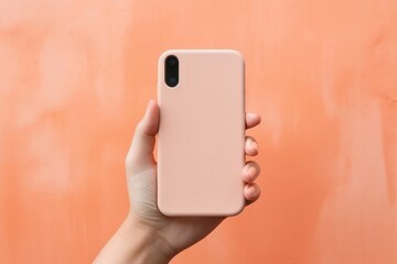 hand holding a mobile phone on pastel peach background with copy space. Phone case mockup of peach fuzz color of the year 2024. 