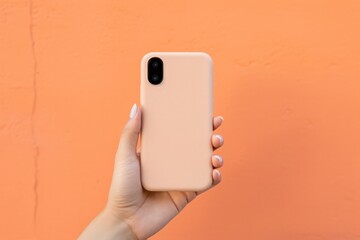 hand holding a mobile phone on pastel peach background with copy space. Phone case mockup of peach...
