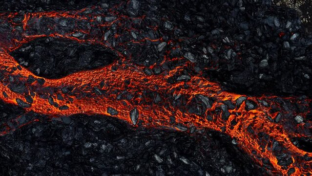 Mesmerizing view of a lava flow, red hot molten liquid streaming over black solid volcanic rocks, aerial directly above shot. Abstract, texture, and background concepts.