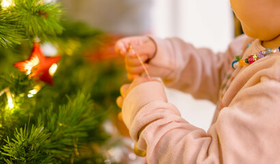 Little girl placing ornaments on the Christmas tree with golden glittering lights.