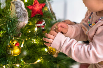 Little girl placing ornaments on the Christmas tree with golden glittering lights.