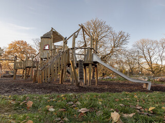 Fototapeta na wymiar The Children's playground with Slide, Rope Net Bridge made of Wooden Tree trunk in acton park. Empty outdoor playground with wooden equipment for children, Space for text, Selective focus.
