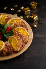 Aerial view of half a Roscón de Reyes with orange and holly, on a wooden plate, on a dark table with Christmas decorations, vertically, typical Spanish Christmas dessert