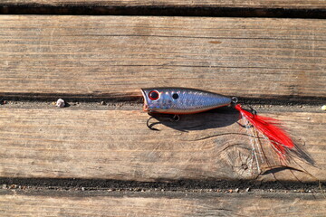 Fishing bait and hook in a shape of a small fish. Wooden background.