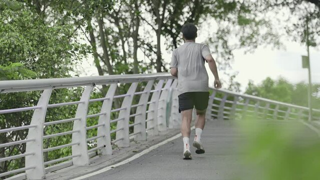 rear view of young asian man jogging running exercising outdoors in park