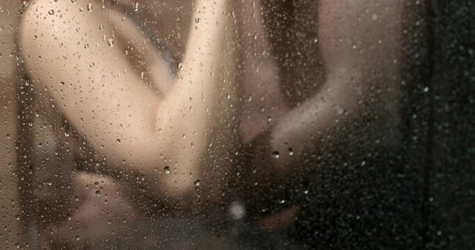 Loving affectionate woman leaned on glass in shower, having intimate moment with boyfriend. Close-up photo of elastic buttocks in black swimsuit rear view. sex, relationships, passion. copy space