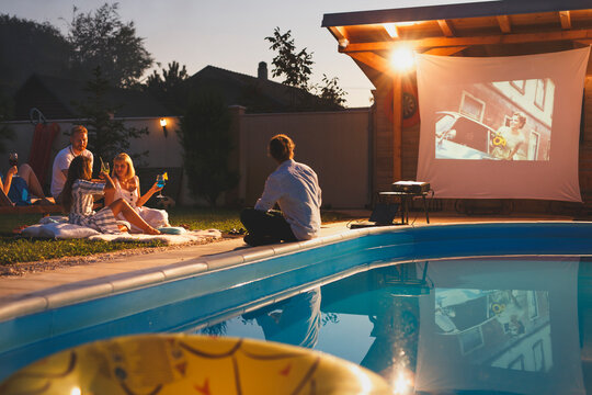 Friends having fun watching a movie by the swimming pool - Powered by Adobe