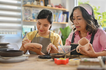 Asian Grandmother and young daughter painting ceramic crockery, Cottage industry with family...