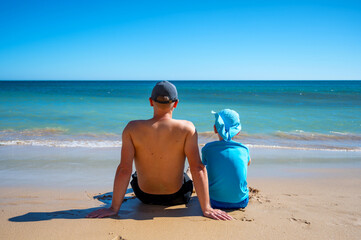 Vater und Sohn genießen gemeinsamen Urlaub am Strand mit Blick Richtung blauem Meer