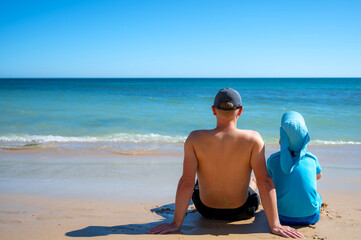 Mann und Kind sitzen nebeneinander am Strand mit Textfreiraum als Hintergrund