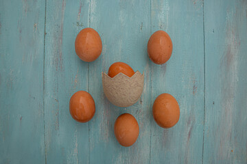 Six eggs on blue vintage wooden background, one of them inside a shell