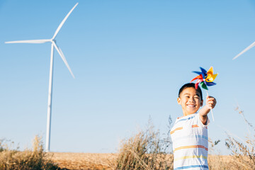Joyful child playing with pinwheel toy near wind turbines celebrates spirit of wind energy. Showcases clean electricity innovation amidst peaceful countryside windmill farm against a bright blue sky.