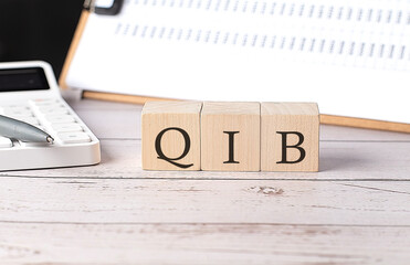 QIB word on a wooden block with clipboard and calculator