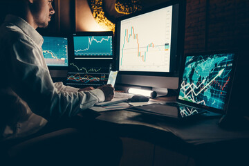 Male trader analyzing stock market data while sitting at office workstation with multiple computers