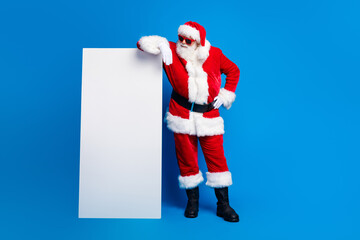 Full length photo of elderly retired man lean on vertical banner wear trendy santa claus costume coat isolated on blue color background