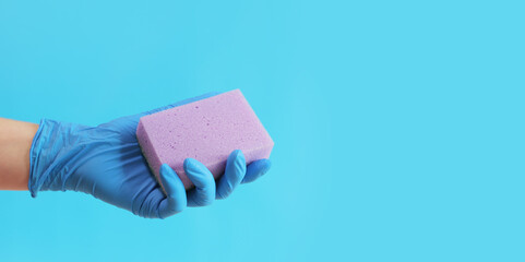 Purple dishwashing sponge in a woman's hand on a blue background. A hand in a latex blue glove holds a sponge for wet cleaning. Professional cleaning. Copy space