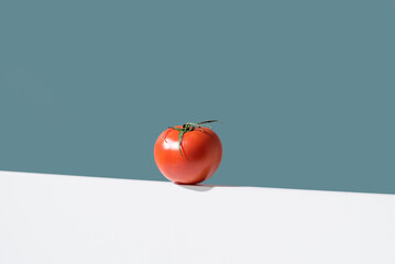 Un tomate rojo fresco sobre un soporte blanco y fondo verde