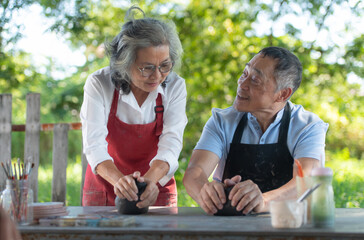 In the pottery workshop, an Asian retired couple is engaged in pottery making and clay painting activities.