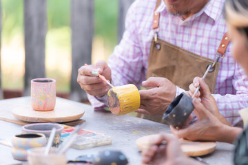 In the pottery workshop, an Asian retired couple is engaged in pottery making and clay painting activities. - obrazy, fototapety, plakaty