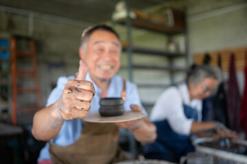 Portrait of senior craftsman working on pottery with thumb up