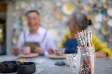 In the pottery workshop, an Asian retired couple is engaged in pottery making and clay painting activities.