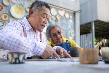 In the pottery workshop, an Asian retired couple is engaged in pottery making and clay painting activities.