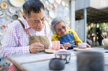 In the pottery workshop, an Asian retired couple is engaged in pottery making and clay painting activities.