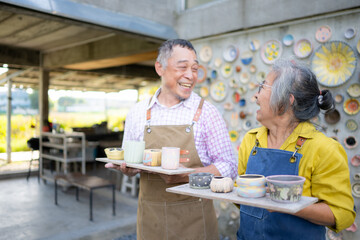 A senior Asian couple enjoys their own hand-painted pottery.