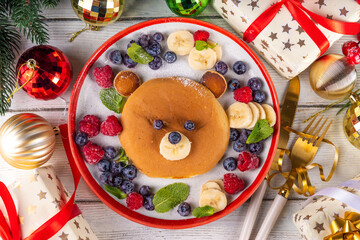 Funny and cute Christmas teddy bear pancakes on a red white plate decorated with fresh berry, fruit and powdered sugar, children's Christmas breakfast or brunch idea