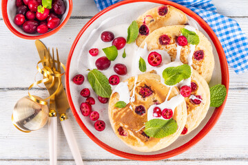 Fototapeta na wymiar Sweet cranberry pancakes for winter breakfast or brunch. Festive Christmas, New Year breakfast dessert with vanilla creamy topping and fresh cranberries, copy space
