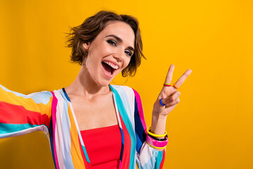 Selfie of young funk smiling girl joking show v sign picture greetings demonstrate retro discotheque isolated on yellow color background