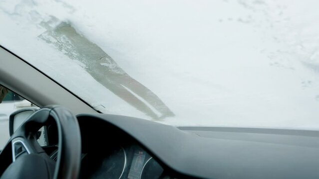 A man scrapes frost off the front window of his car on a cold winter morning