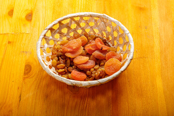 Dried apricots and raisins in a wicker plate on a wooden table