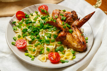 Farfalle pasta with grilled chicken wings garnished with cherry tomatoes and green onions