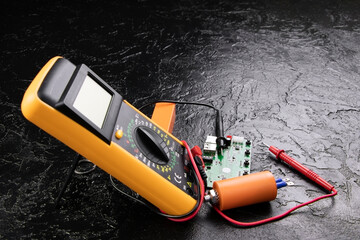 Digital multi-meter with probes on a black stone background. Multitester and microcircuit. Voltage...