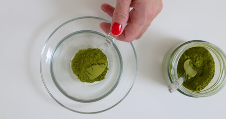 Woman is putting matcha powder in glass cup by the spoon