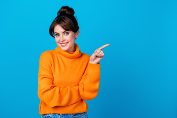 Photo of confident pretty woman dressed orange sweater pointing finger empty space isolated blue...