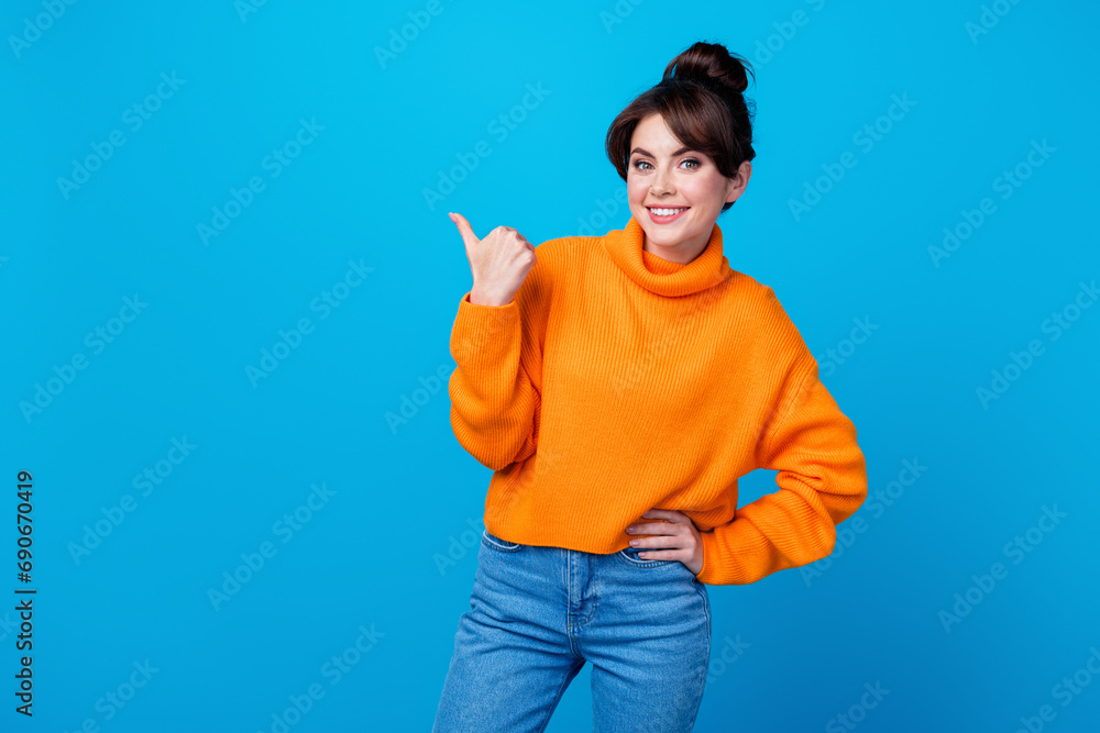 Sticker Photo of adorable cheerful woman dressed orange sweater showing thumb empty space isolated blue color background