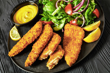 breaded fish fillet with salad on black plate