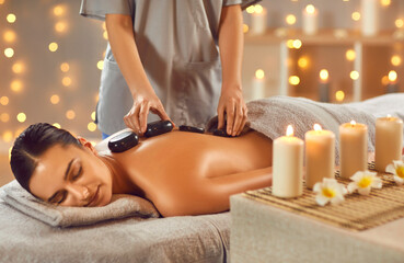 Serene attractive brunette woman getting hot stone massage in spa salon. Beautiful girl lying on...