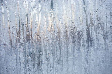 Frozen vertical water streaks and drops on window. Magic of nature. Christmas or winter background.