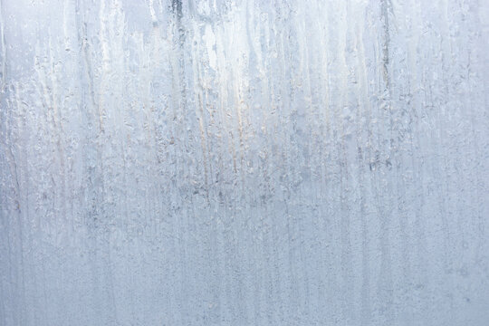 Winter window with frozen vertical water stripes. Frosty patterns on winter iced white window glass - Powered by Adobe