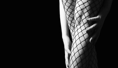 Beautiful female legs in mesh tights in dark lighting. Close-up - obrazy, fototapety, plakaty