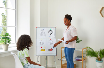 School counselor or psychologist working with a little girl, standing by a white board with...