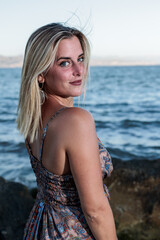 very pretty blonde woman in dress posing on the beach with the sea in the background