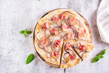 French tarte flammkuchen with cream cheese, onion and bacon on a board on the table. Top view