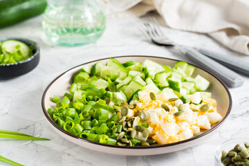 Fresh salad of cucumber, boiled egg and green onion on a plate on the table. Ketogenic diet. - obrazy, fototapety, plakaty