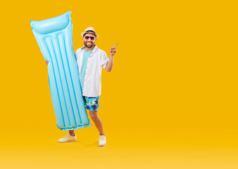 Cheerful man with inflatable swimming mattress pointing at copy space on orange background. Cheerful Caucasian guy in sunglasses and beachwear is advertising summer product with smile. Banner. - obrazy, fototapety, plakaty