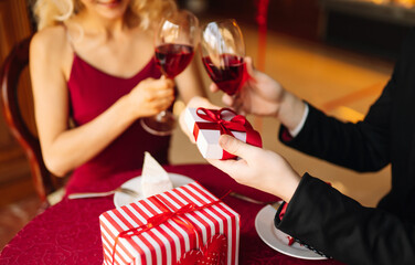 A young couple in love exchanges gifts for Valentine's Day in a cafe at the table. Handsome man and...