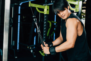 Muscular young man exercising with a pull down cable machine, targeting his triceps and back...